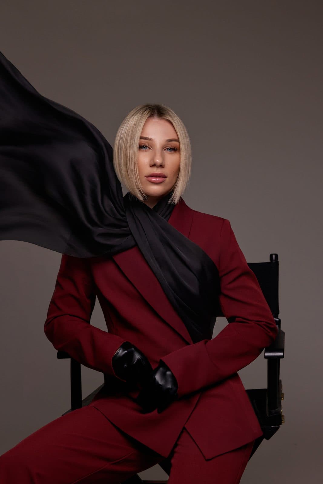 Irma Lion seated in a director's chair, a black silk scarf in motion