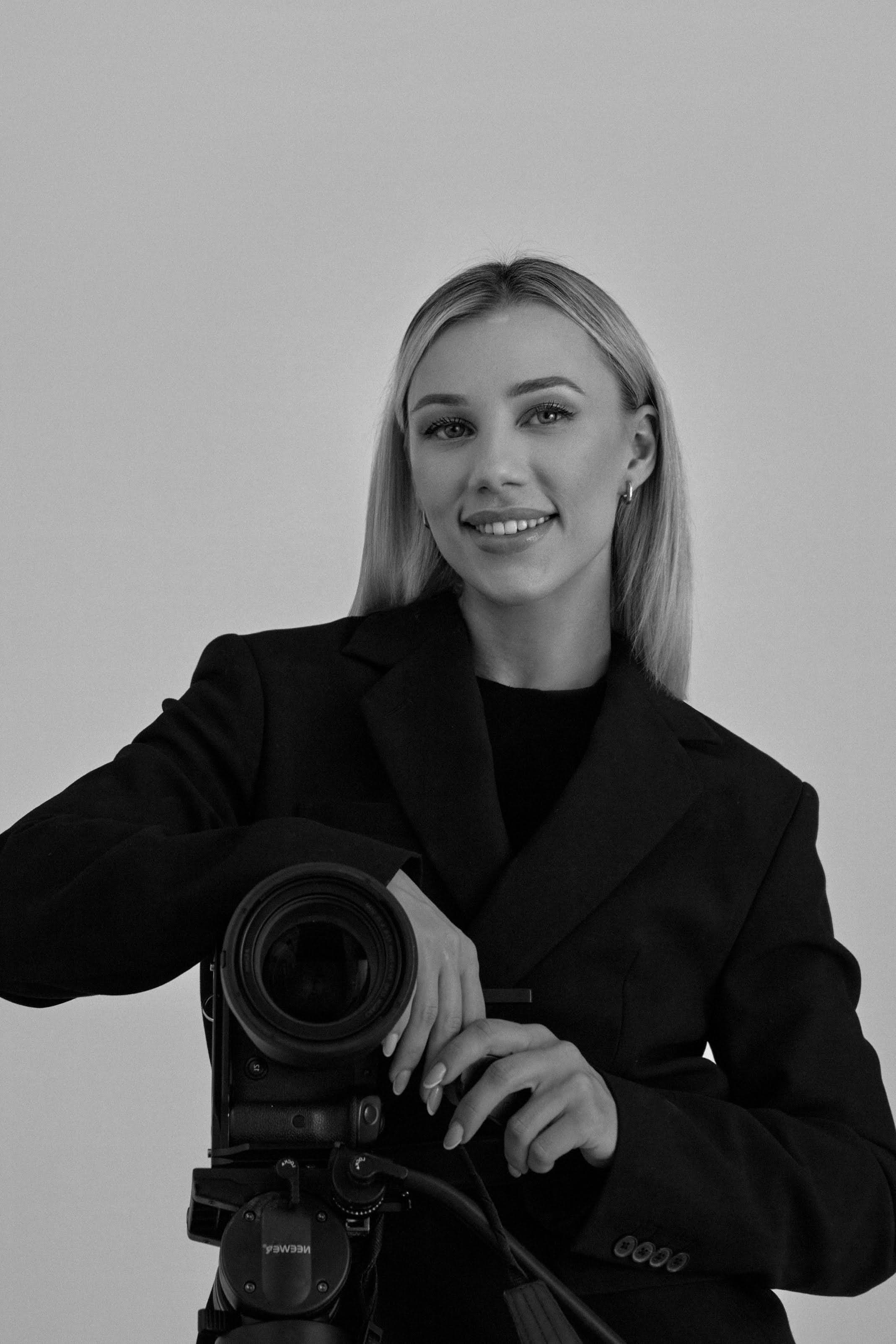 Irma Lion in a black blazer, resting on a medium-format camera